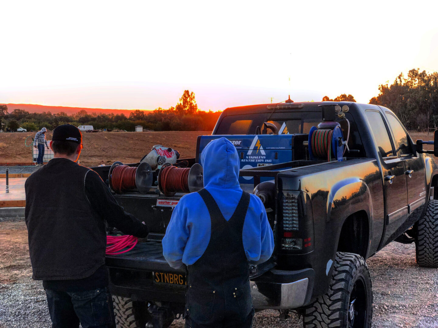 Two men standing next to a truck with the back of it.